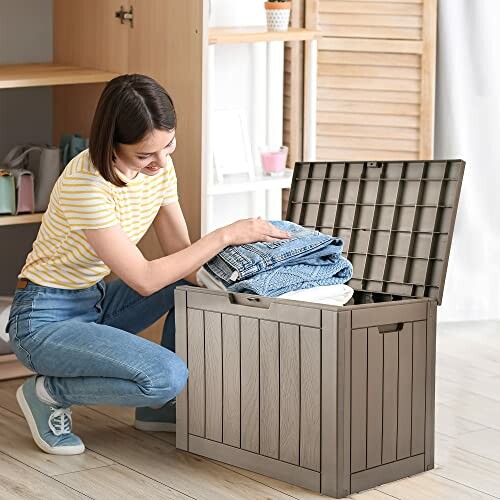 Woman placing clothes in a storage box with lid open.